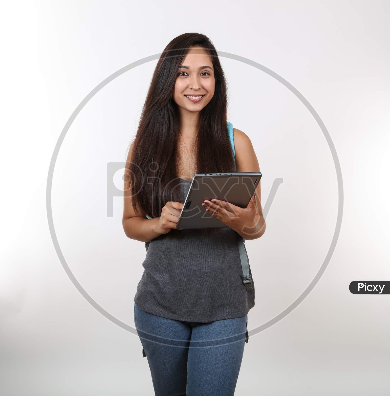 An Attractive Student Smiles Wearing Backpack As She Uses Her Tablet.
