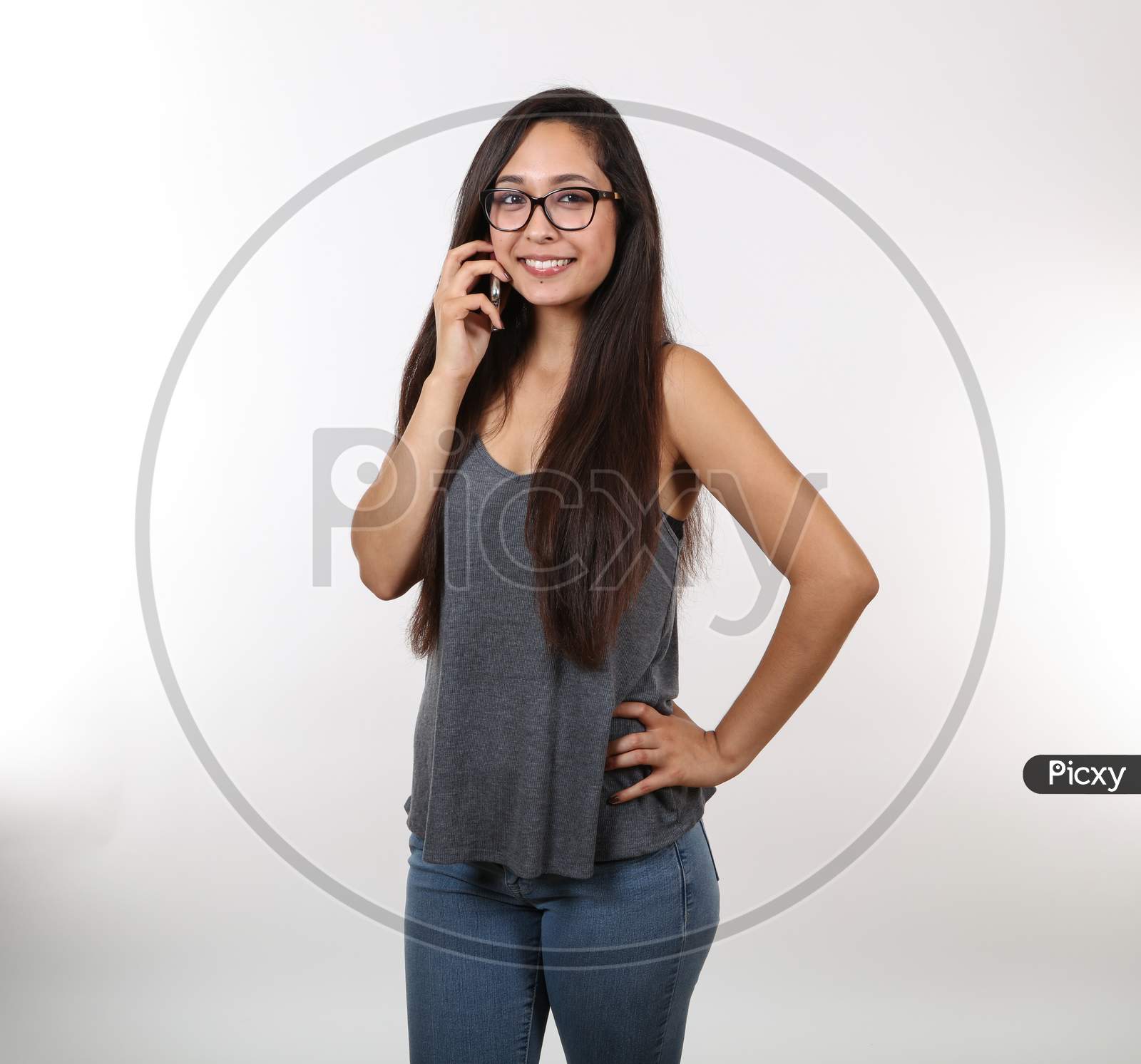 A Pretty Young Lady In Blue Jeans And A Grey Tank Top Wearing Glasses.  Talking On The Phone.