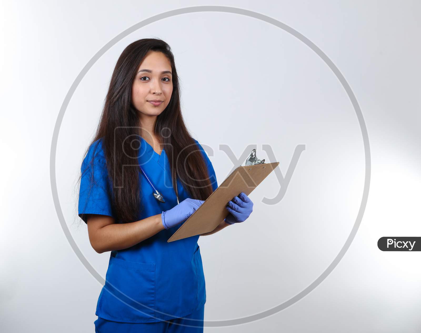 A Young Attractive Nurse In Blue Scrubs Points At Her Clipboard.