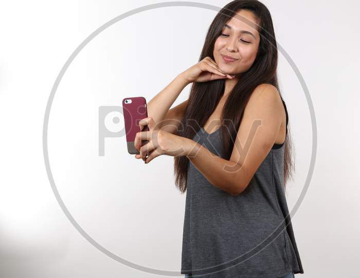 An Attractive Latina Wearing Glasses And A Grey Shirt Smiles As She Holds Her Cell Phone Up To Take A Picture.