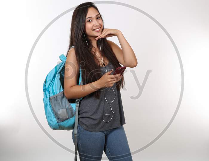 An Attractive Hispanic Student Wearing A Blue Backpack And Earphones Smiles As She Strikes A Pose.