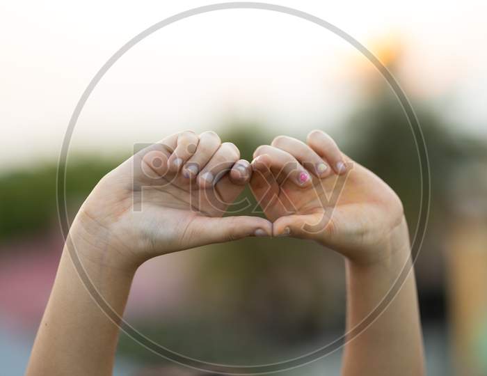 Child Making Heart Shape With Hand Outdoors During Sunset