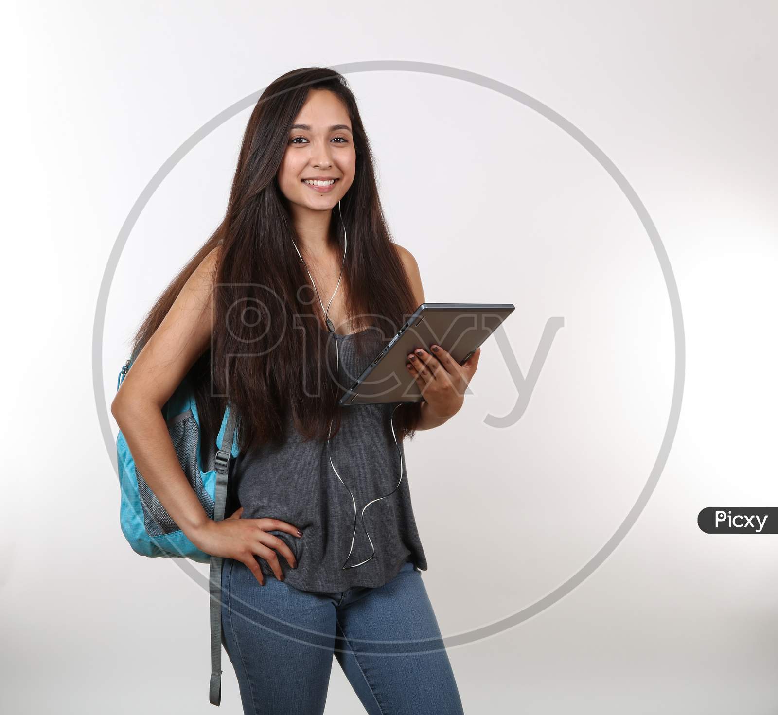 An Attractive College Student Smiles At The Camera As She Holds Her Tablet And Listens To Music.
