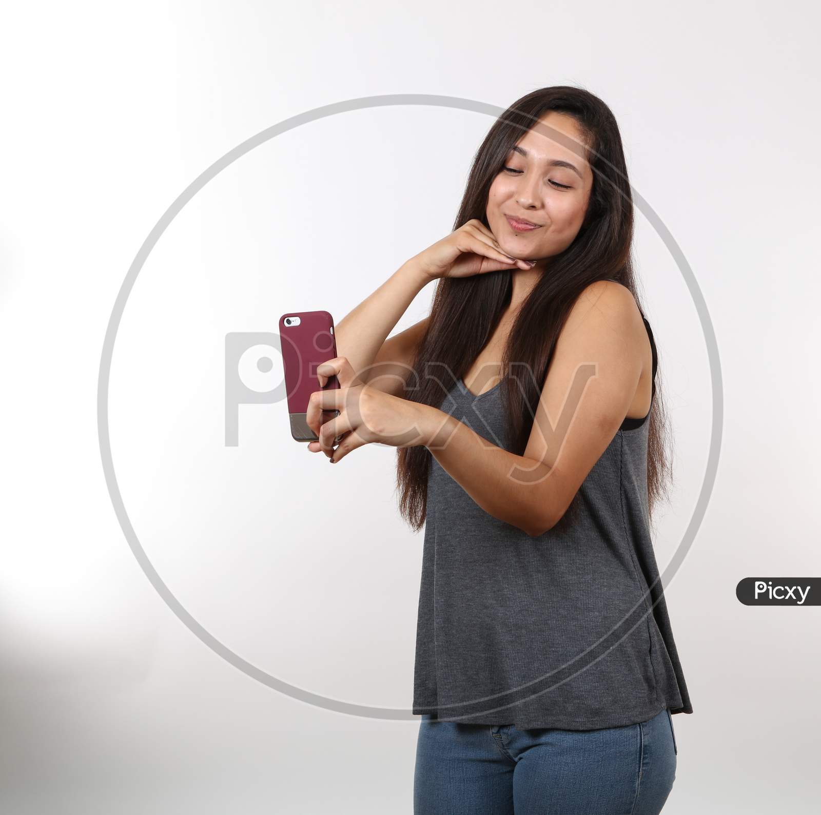 An Attractive Latina Wearing Glasses And A Grey Shirt Smiles As She Holds Her Cell Phone Up To Take A Picture.