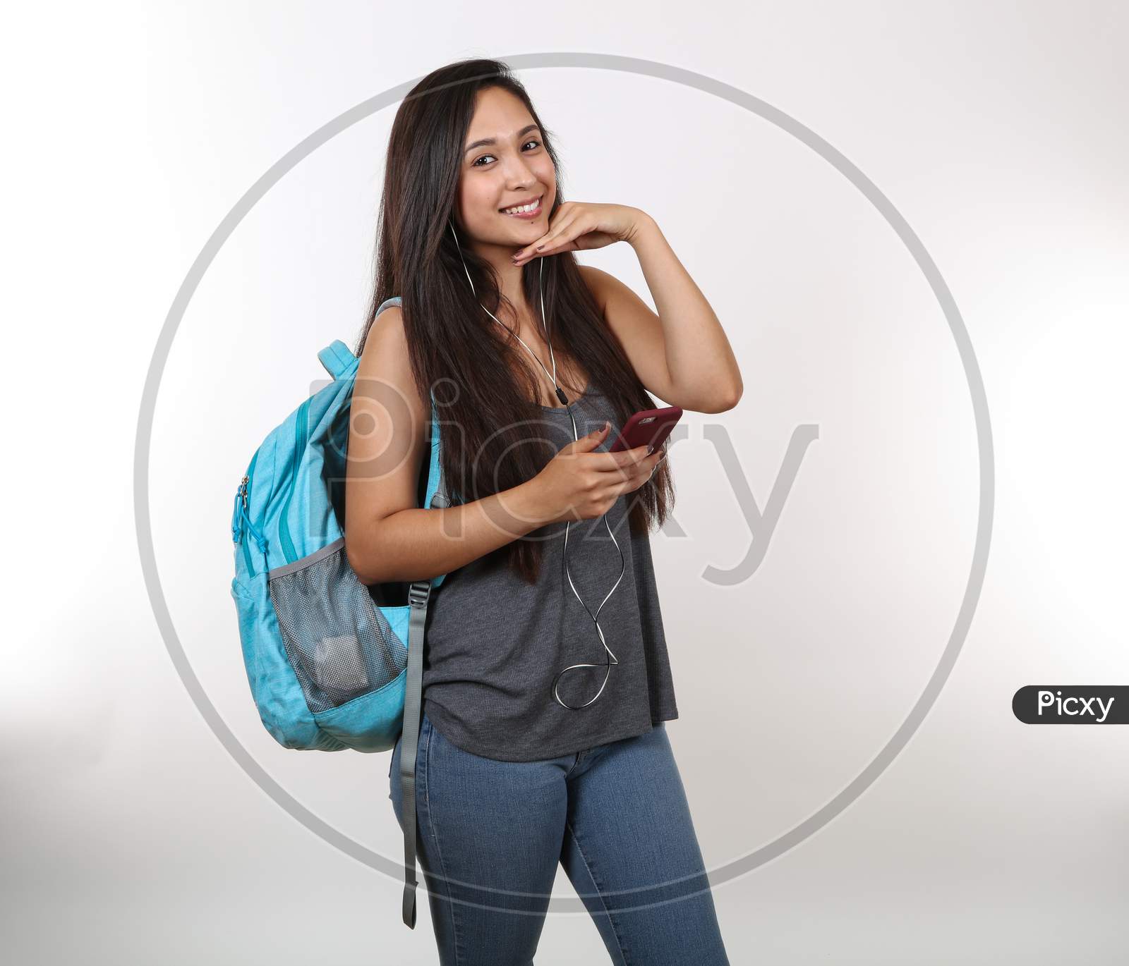 An Attractive Hispanic Student Wearing A Blue Backpack And Earphones Smiles As She Strikes A Pose.