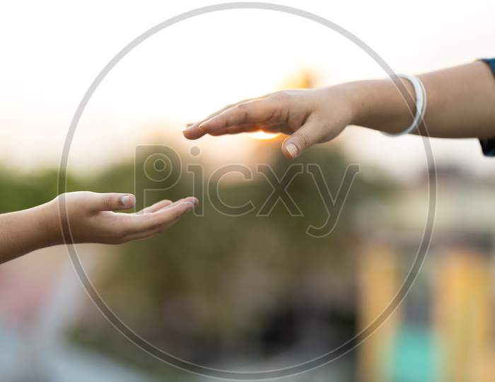 Woman And Child Reaching Out To Hold Hands Outdoors At Sunset