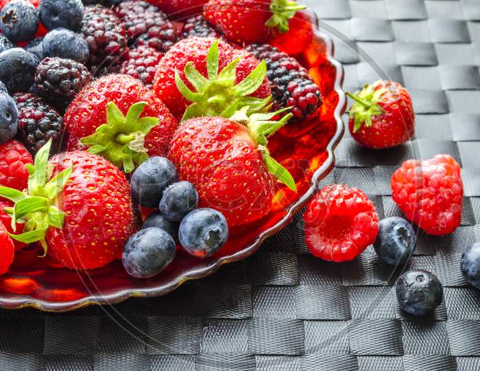 A shot of a plate of fresh summer fruit on a dark woven mat.