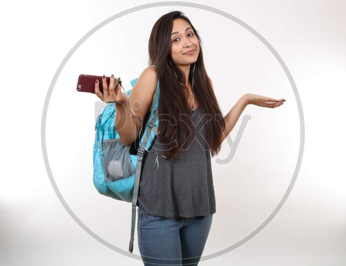 A Young Latina Student Wearing A Blue Backpack, Holding Her Phone Shrugs Her Shoulders.  Listening To Music.