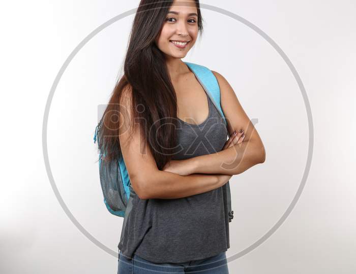 A Young Female Student In Casual Clothes Crosses Her Arms As She Smiles And Holds Her Backpack.