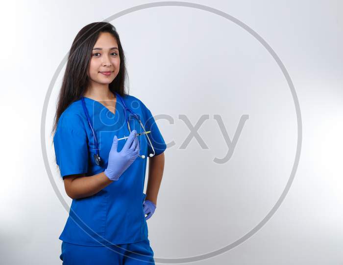 A Young Female Nurse In Blue Scrubs Hold A Syringe.