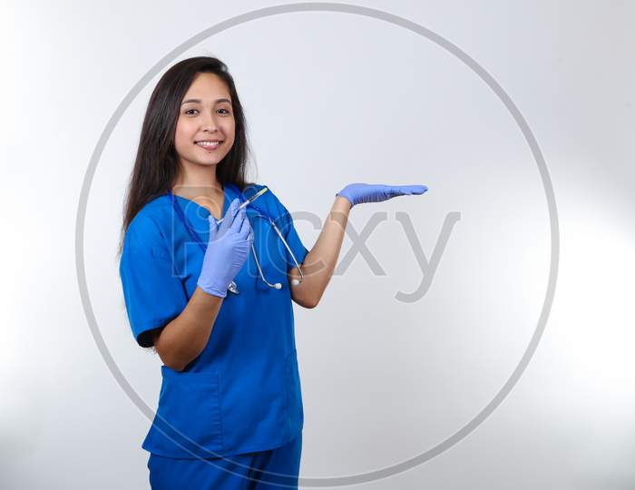 An Energetic Nurse In Scrubs Holds A Syringe And Her Hand Up.