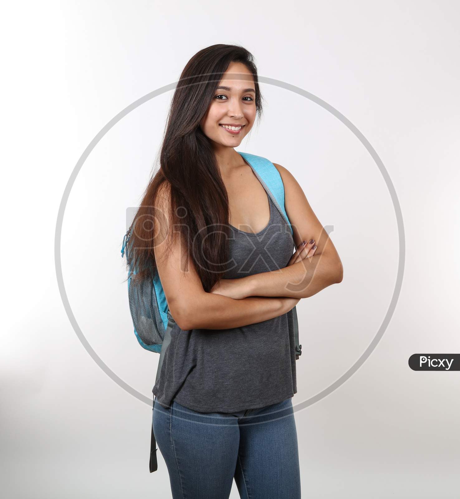 A Young Female Student In Casual Clothes Crosses Her Arms As She Smiles And Holds Her Backpack.