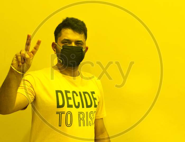 Indian guy wearing mask with victory sign to stop covid spread with yellow background and open Space for text