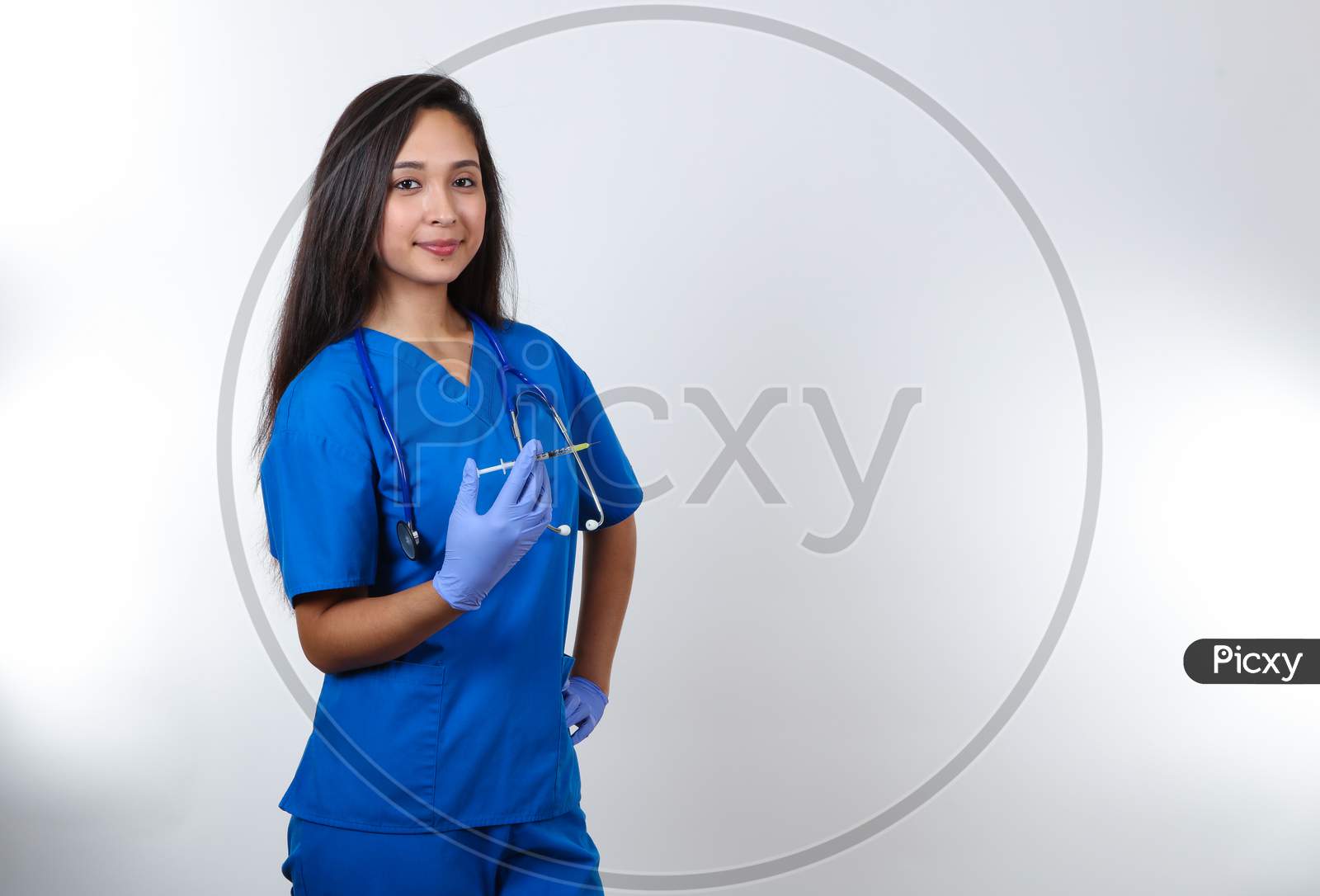 A Young Female Nurse In Blue Scrubs Hold A Syringe.