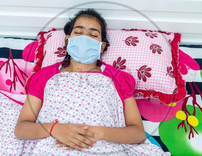Young Brunette Girl With Covid-19 Lies In Bed At Home Wearing A Medical Mask. Quarantine Self-Isolation Concept
