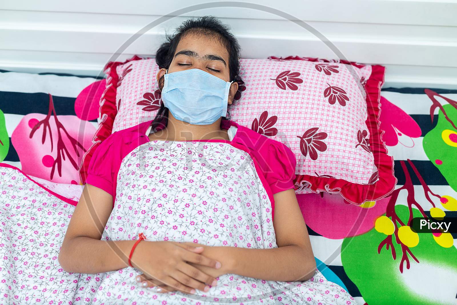 Young Brunette Girl With Covid-19 Lies In Bed At Home Wearing A Medical Mask. Quarantine Self-Isolation Concept