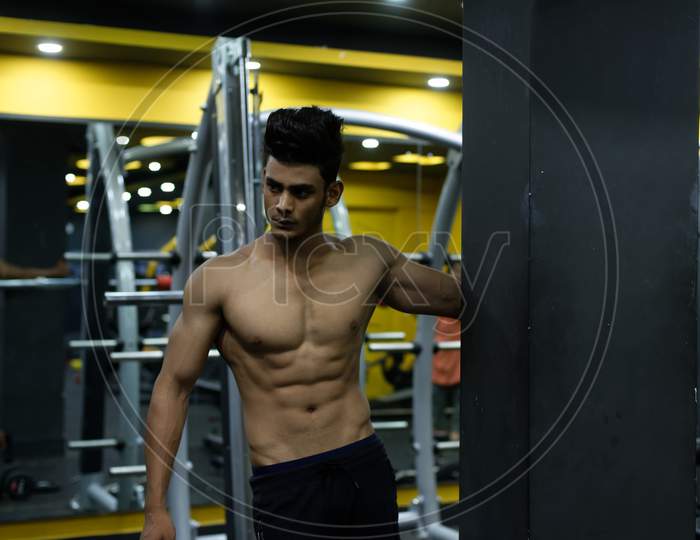 Portrait of an young and handsome Indian Bengali brunette man with muscular body doing exercise in a multi gym. Indian lifestyle