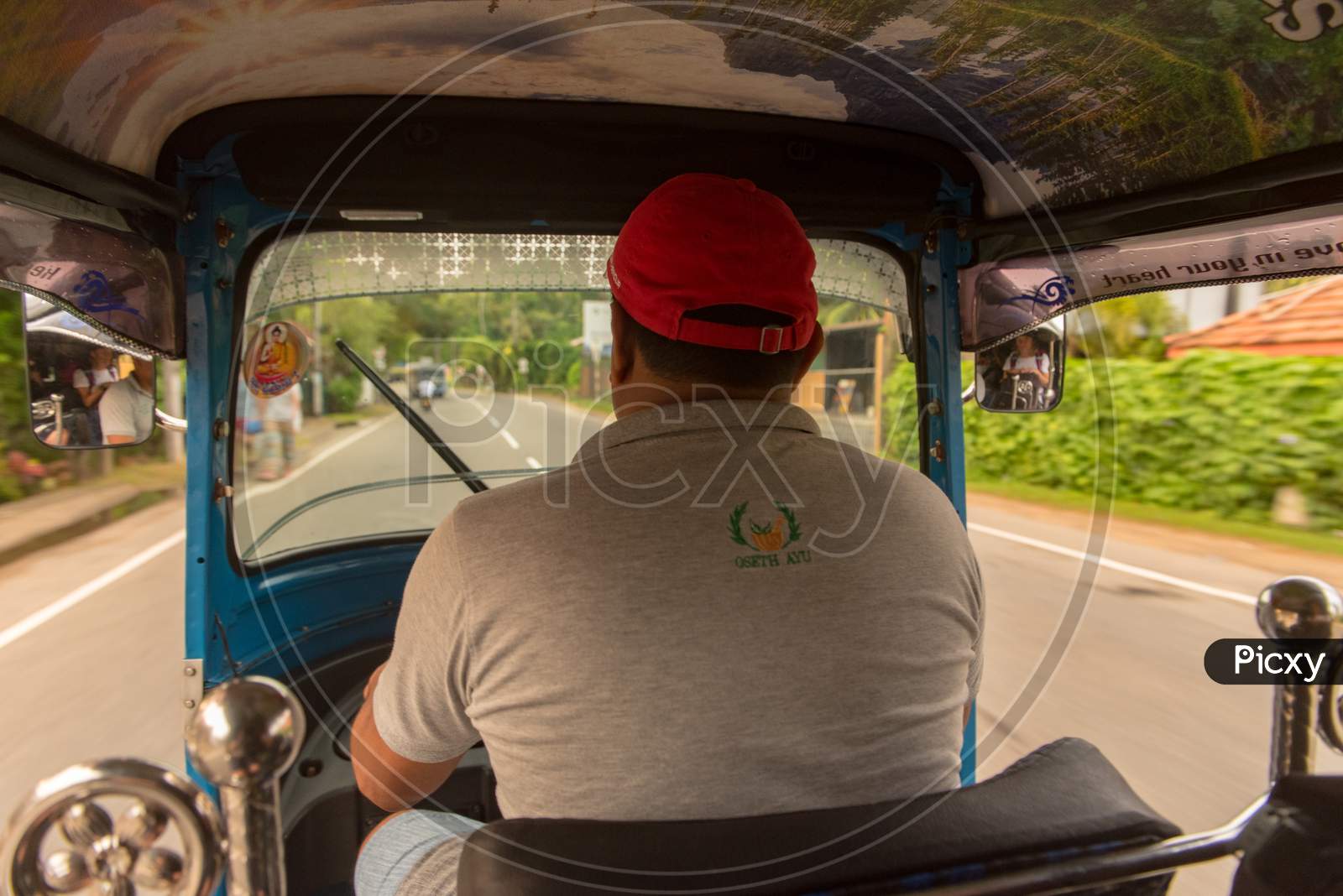 Bentota, Sri Lanka - Nov 16, 2019: The Sunny View From Inside The Tuk Tuk Taxi, Behind The Driver As It Is Driven Along A Country Road With The Passenger'S Reflection Visible In The Wing-Mirror.