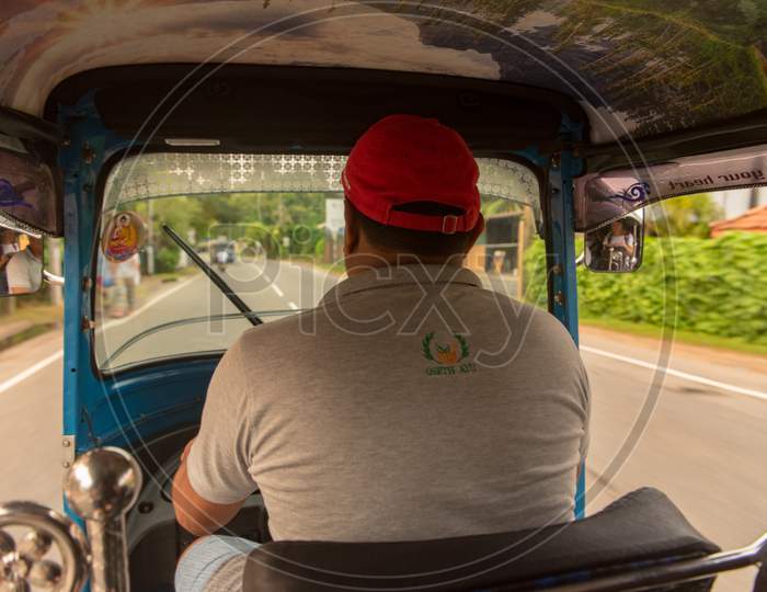Bentota, Sri Lanka - Nov 16, 2019: The Sunny View From Inside The Tuk Tuk Taxi, Behind The Driver As It Is Driven Along A Country Road With The Passenger'S Reflection Visible In The Wing-Mirror.