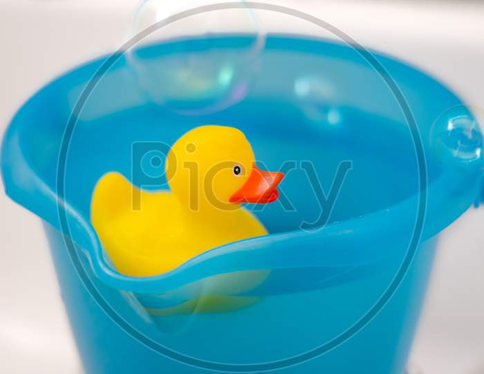 Yellow rubber duck in a blue bucket full of water with soap bubbles