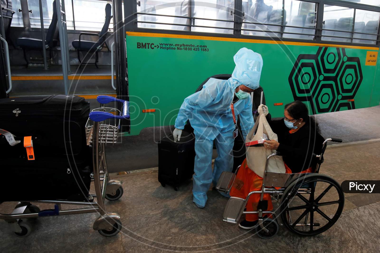 An airport worker helps a woman in a wheelchair to be taken to a quarantine centre in the city at the Kempegowda International Airport in Bangalore, India, May 11, 2020. Three hundred twenty six passengers stranded in the UK due to the covid-19 lockdown arrived in an Air India flight.