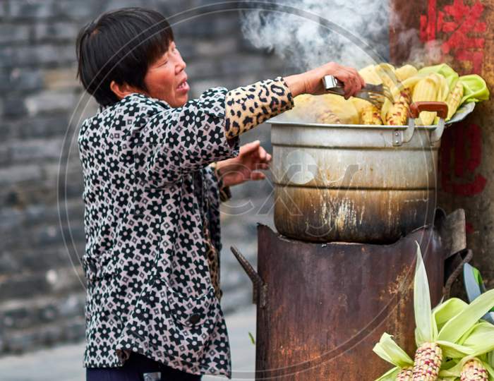Woman Cooking Corn Clips On A Street Food Stall In Qufu, Birthplace Of Philosopher Confucius, Shandong Province, China