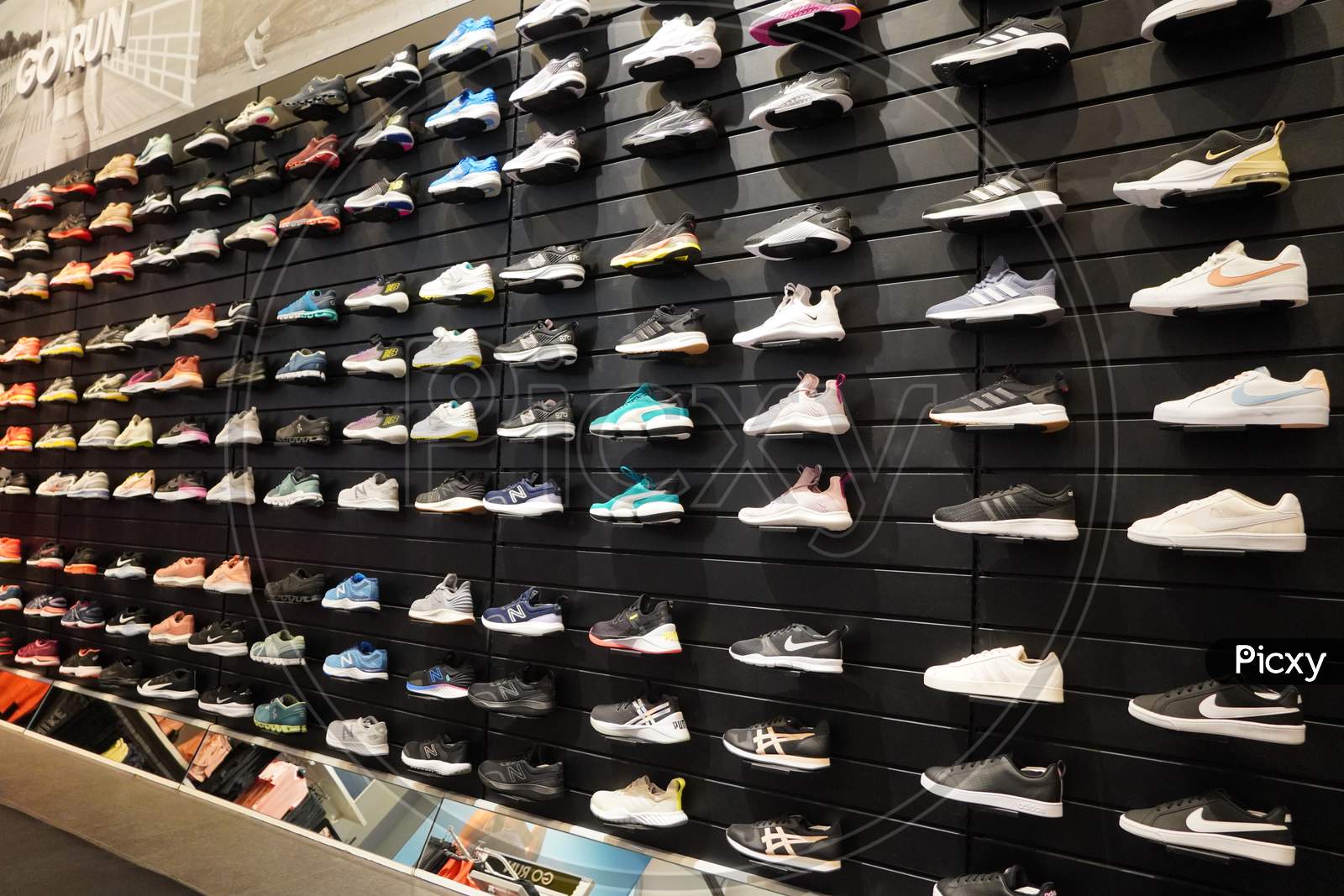 Shop Display Of A Lot Of Sports Shoes On A Wall. A View Of A Wall Of Shoes Inside The Store. Modern New Stylish Sneakers Running Shoes For Men And Women.