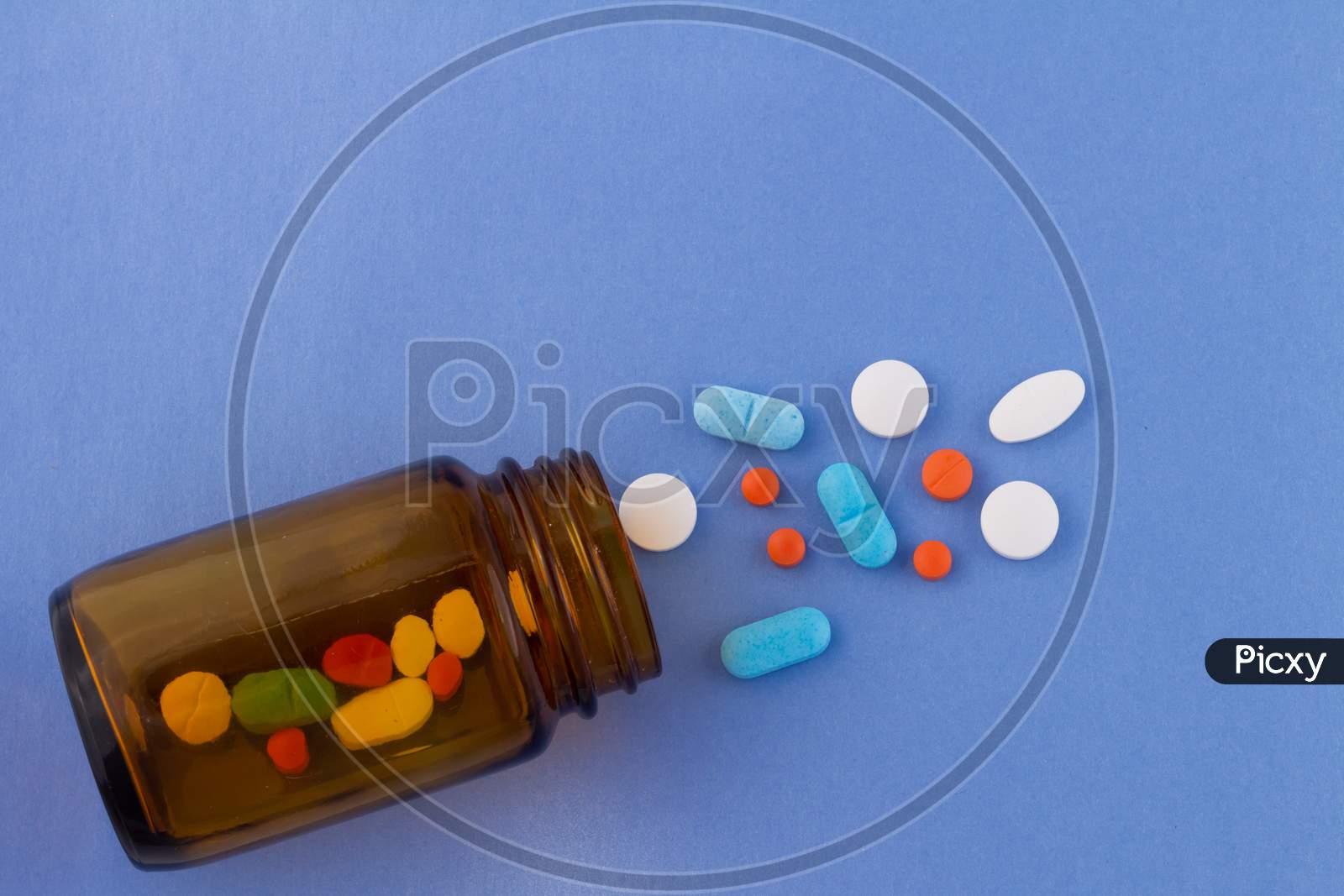 Colored Pills On A Light Blue Background Next To A Glass Bottle Containing Drugs. Drugs For Use In Humans.