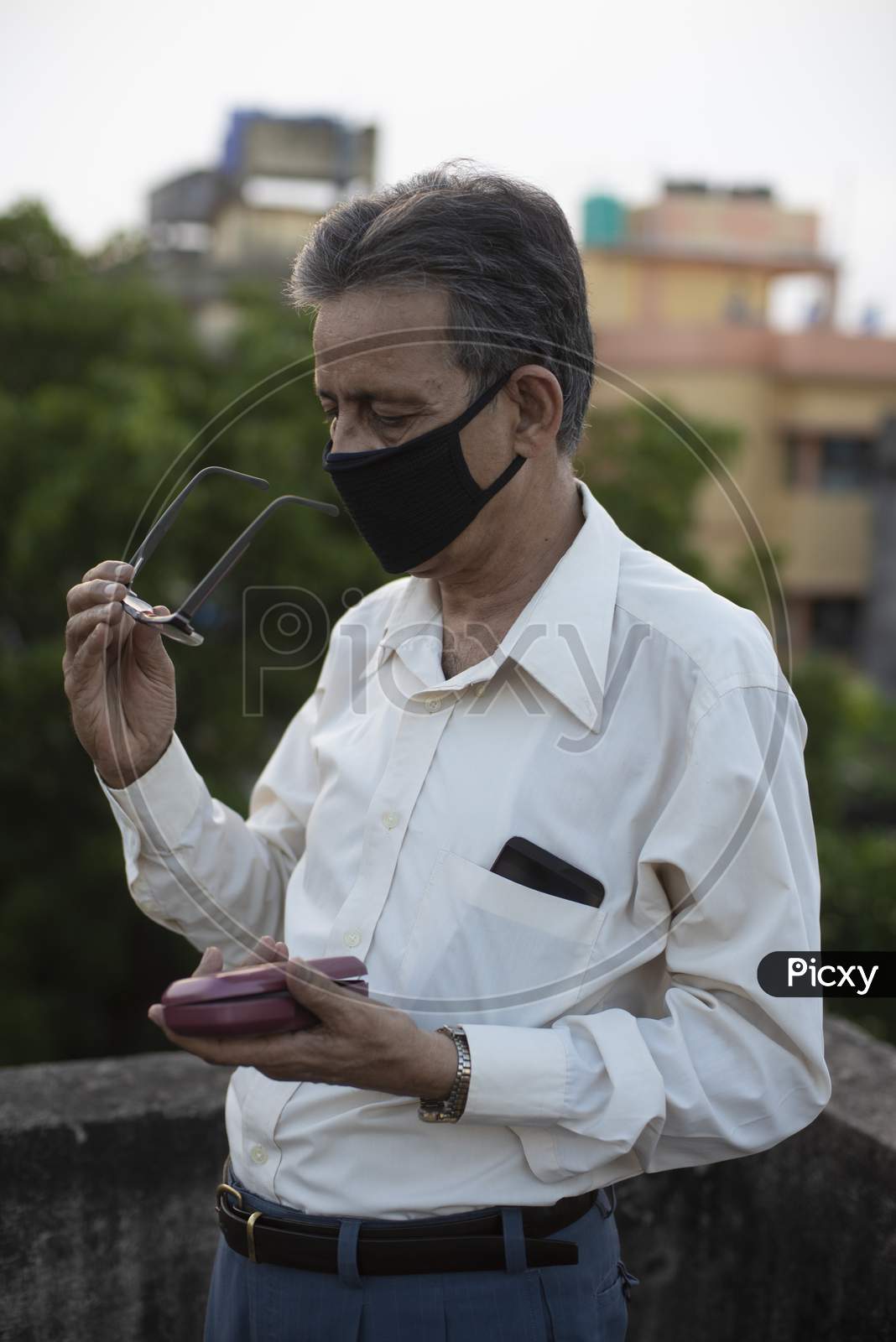 Image of portrait of an Indian old man with corona preventive mask removing  his spectacles on a rooftop during sunset in home isolation.Indian  lifestyle, disease and home quarantine.-YL996670-Picxy