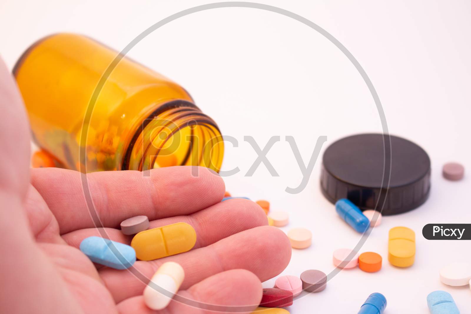 Medications In The Form Of Pills And Capsules On A White Background. Brown Glass Vessel. Hand Of A Man Holding Colored Pills.