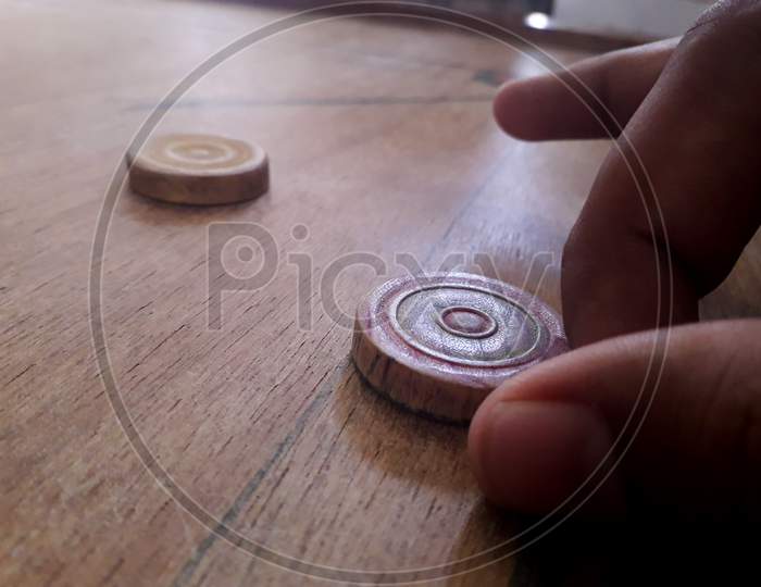 A male person hitting wooden coins by striker in carrom competition on an old carrom board
