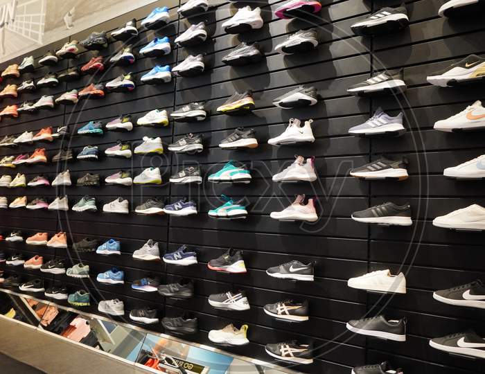 Shop Display Of A Lot Of Sports Shoes On A Wall. A View Of A Wall Of Shoes Inside The Store. Modern New Stylish Sneakers Running Shoes For Men And Women.