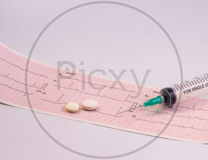 Electrocardiogram Strip With A Syringe And Its Needle And A Pair Of White Pills. Free Space To Write. Concept Of Cardiovascular Health.