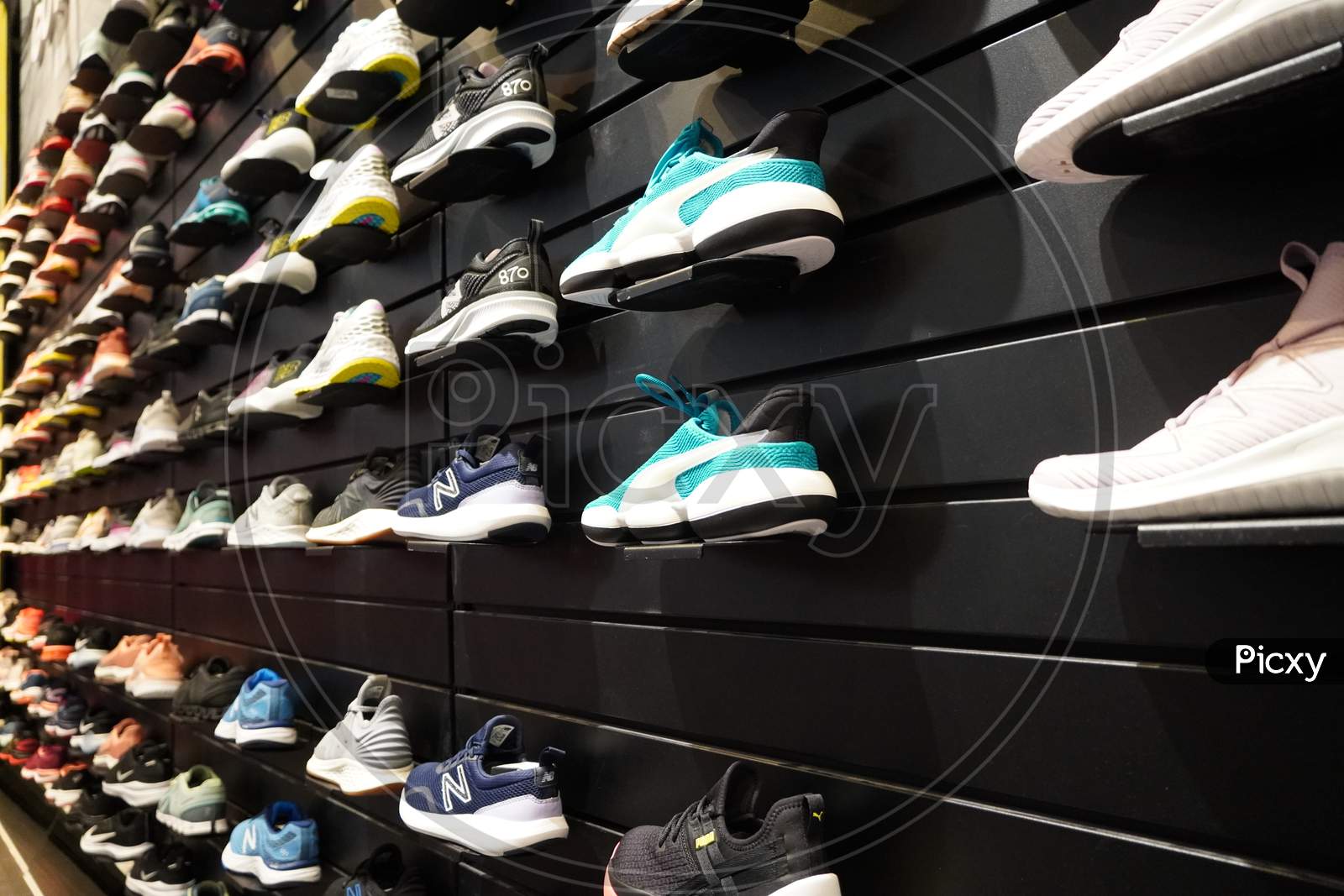 Shop Display Of A Lot Of Sports Shoes On A Wall. A View Of A Wall Of Shoes Inside The Store. Modern New Stylish Sneakers Running Shoes For Men And Women