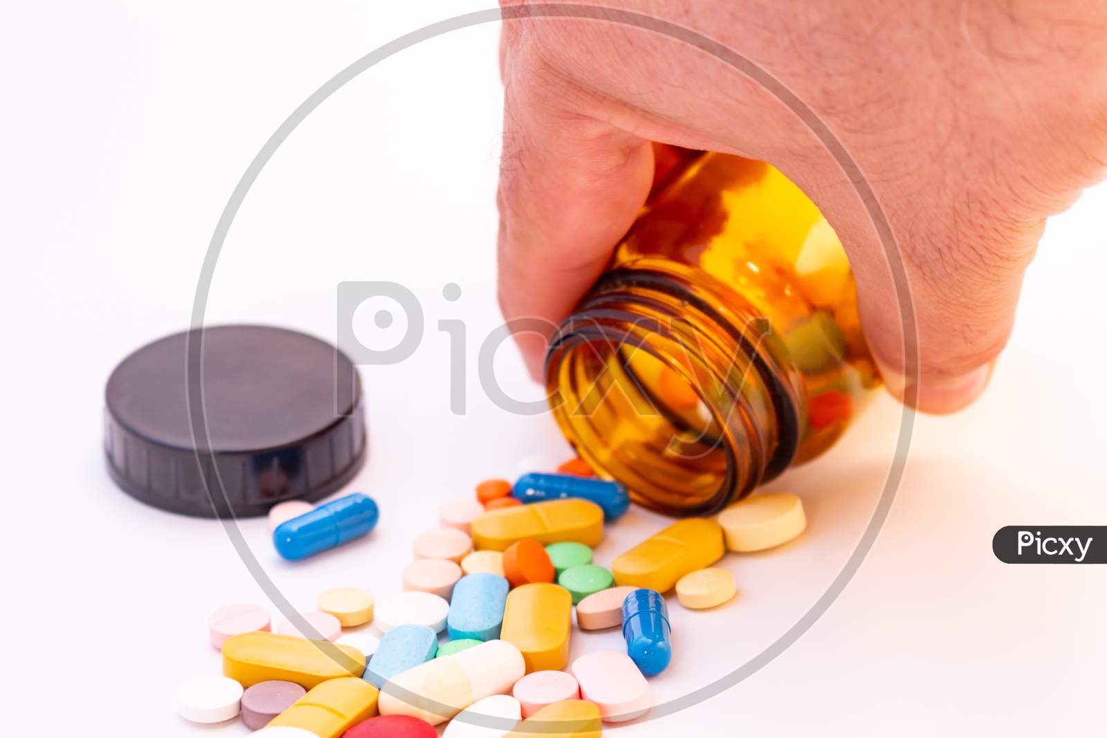 Medications In The Form Of Pills And Capsules On A White Background. Hand Of A Man Holding A Brown Glass Jar.