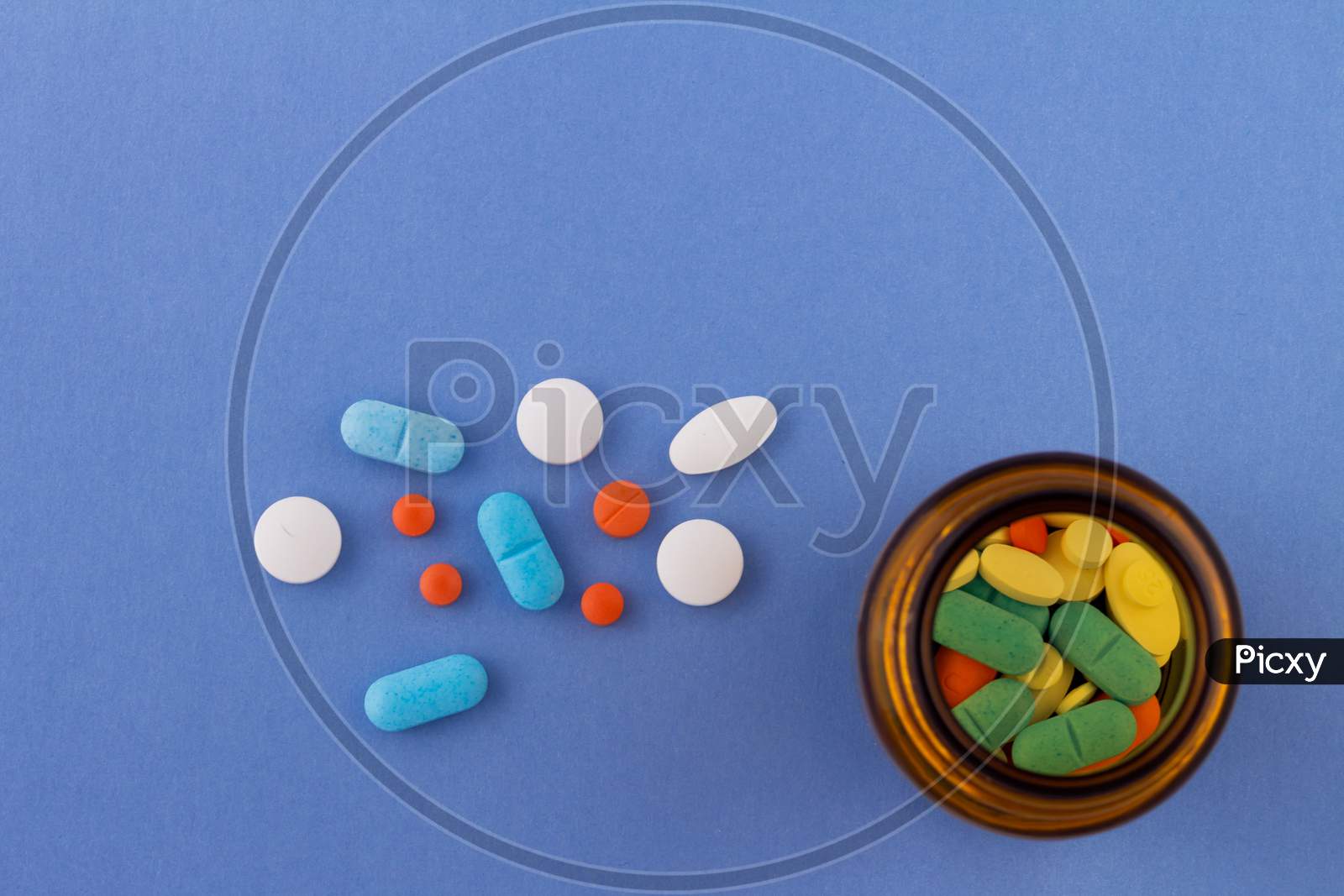 Colored Pills On A Light Blue Background Next To A Glass Bottle Containing Drugs. Drugs For Use In Humans.