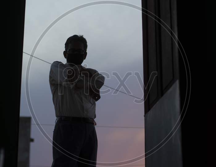 Low angle silhouette portrait of an Indian old man with corona preventive mask on a rooftop during sunset in home isolation.Indian lifestyle, disease and home quarantine.