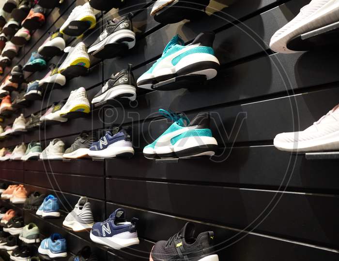 Shop Display Of A Lot Of Sports Shoes On A Wall. A View Of A Wall Of Shoes Inside The Store. Modern New Stylish Sneakers Running Shoes For Men And Women