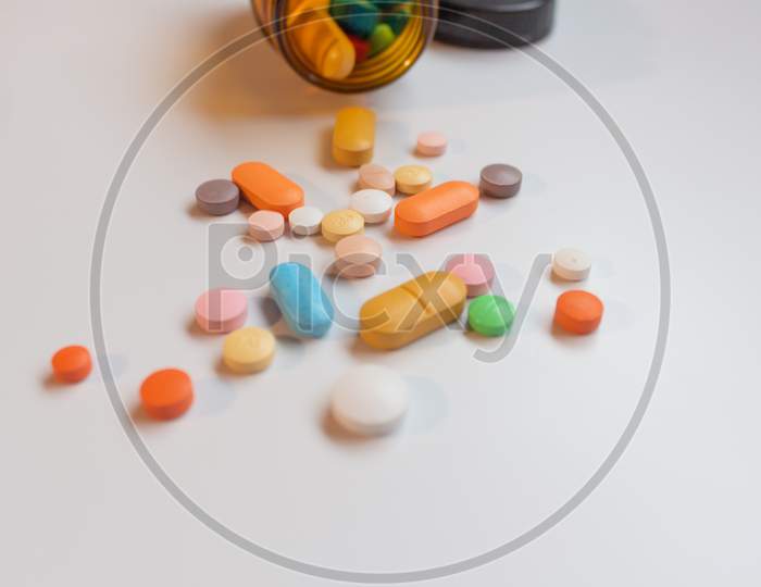 Medications In The Form Of Pills And Capsules On A White Background. Brown Glass Vessel.