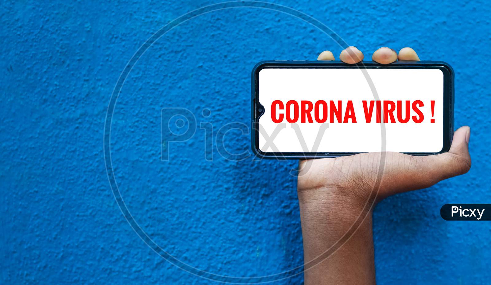 Corona Virus / Covid-19 Wording On Smart Phone Screen Isolated On Blue Background With Copy Space For Text. Person Holding Mobile On His Hand And Showing Front Of The Screen For Corona Virus Wording.