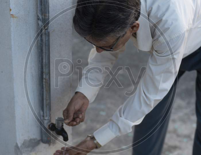 Portrait Of An Indian Old Man Washing His Hand In A Tap Water On A Rooftop During Sunset In Home Isolation.Indian Lifestyle, Disease And Home Quarantine.