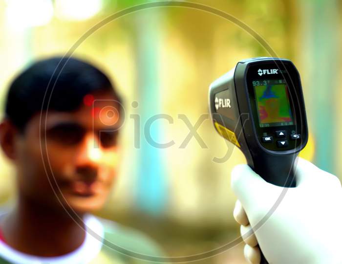Ludhiana, Punjab / India - May 09 2020: Checking a man is temperature with an electronic thermometer. Thermometer in focus, face blurry in the background. Coronavirus, Covid-19 protection.