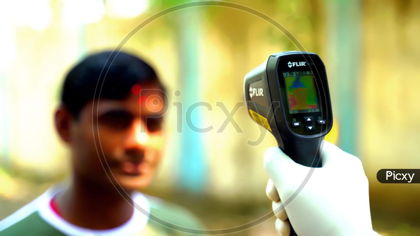 Ludhiana, Punjab / India - May 09 2020: Checking a man is temperature with an electronic thermometer. Thermometer in focus, face blurry in the background. Coronavirus, Covid-19 protection.