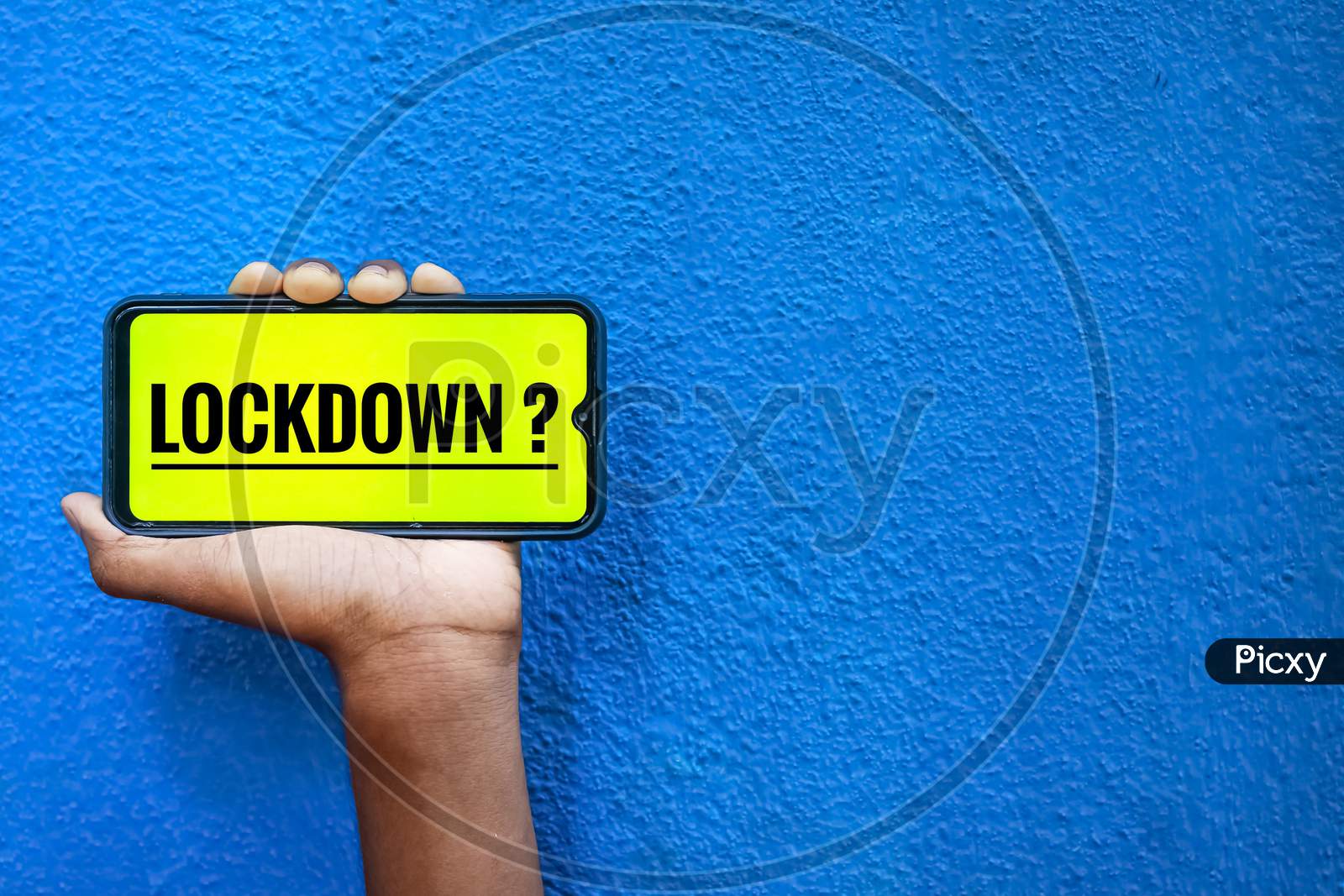 Lock Down Wording For Covid-19 On Smart Phone Screen Isolated On Blue Background With Copy Space For Text. Person Holding Mobile On His Hand And Showing Front Of The Lock Down Corona Virus Screen.
