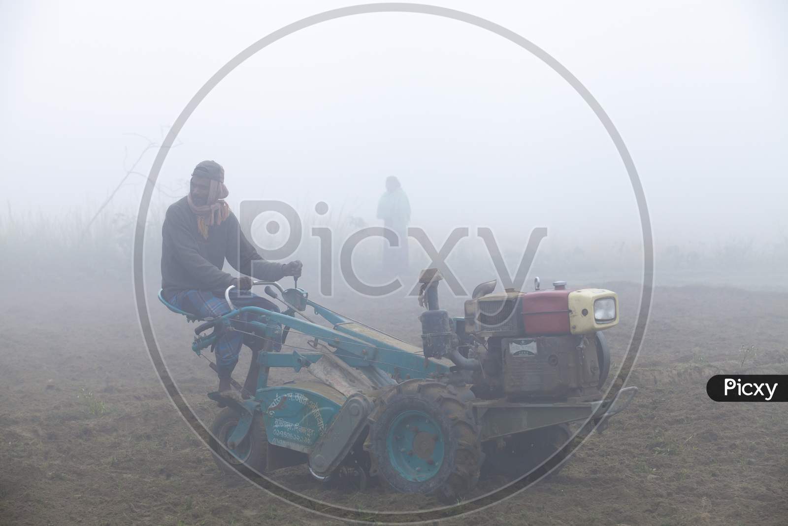 Bangladesh – January 06, 2014: On A Foggy Winter Morning, A Farmer Is Plowing His Land With A 2-Wheel Tractor At Ranisankail, Thakurgaon.