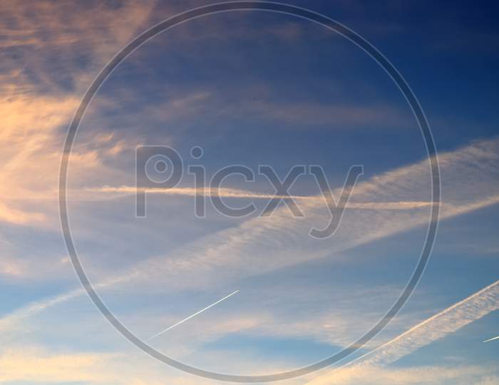 Aircraft condensation contrails in the blue sky inbetween some clouds