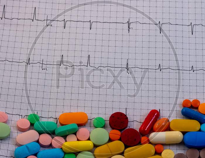 Pills And Medicines Of Different Colors And Sizes On An Electrocardiogram. Drugs For Human Consumption.