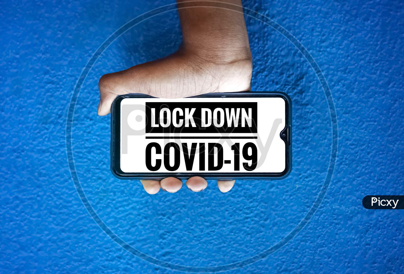 Lock Down Covid-19 Wording On Smart Phone Screen Isolated On Blue Background With Copy Space For Text. Person Holding Mobile On His Hand And Showing Front Of The Lock Down Corona Virus Screen.