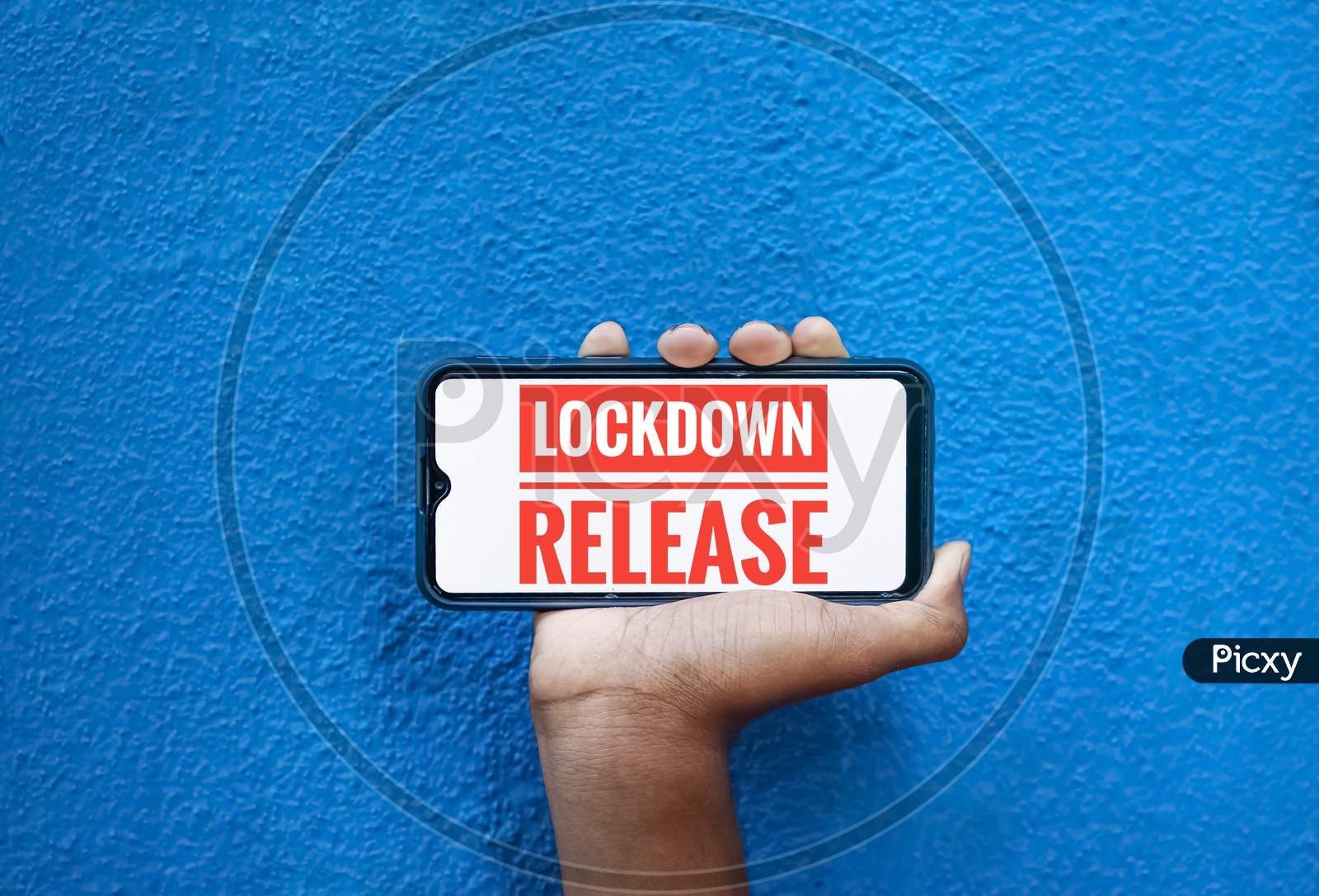Lock Down Release Wording On Smart Phone Screen Isolated On Blue Background With Copy Space For Text. Person Holding Mobile On His Hand And Showing Front Screen. Lock Down Release For Corona Virus .