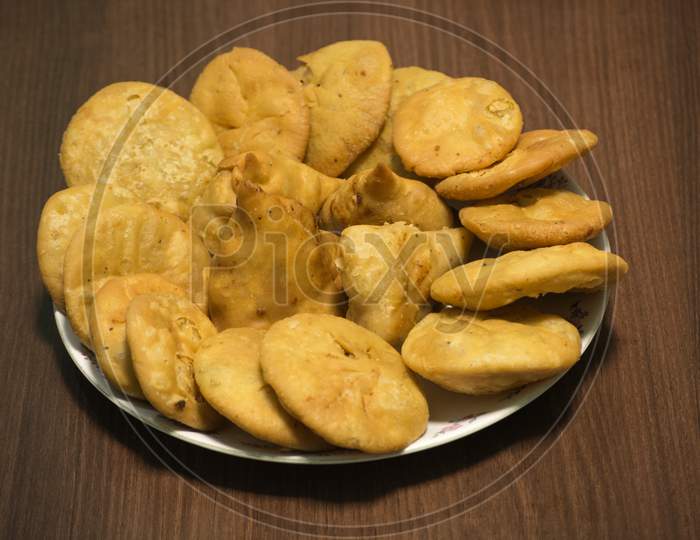Samosa and matthi (mathari/kachori) Indian dish made of fine wheat flour stuffed with potato mesh served in glass dish with wooden background.
